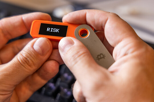 hardware Bitcoin wallet in a hands with message RISK on screen