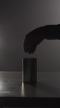 Vertical video silhouette of a hand dropping a coin into a metallic tin can, symbolizing charitable giving, poverty relief, and financial support for those in need during times of economy crisis