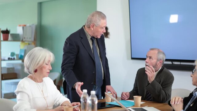 Irritated elderly male boss reprimanding upset subordinates sitting at table in office meeting room, expressing dissatisfaction with work . High quality 4k footage