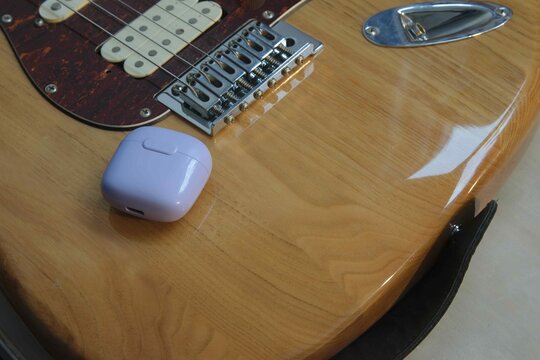 Guitar with earbuds placed on the body, seen indoors with soft lighting