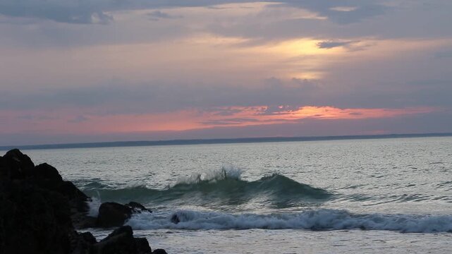 Dramatic evening red sky with the sun rays crossing the clouds. Harmony of meditation near the beautiful sea waves of Normandie and Bretagne. The golden and blue hour of the sunset.