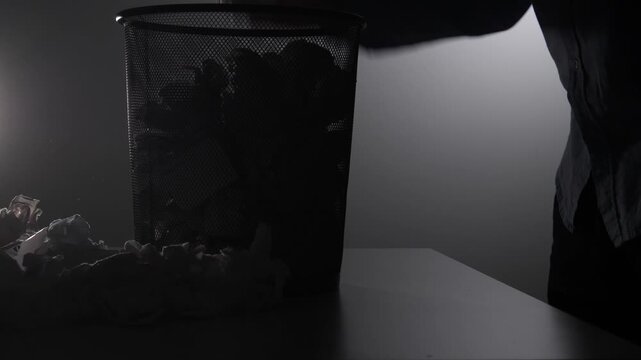 Person discarding crumpled paper into a mesh waste bin, symbolizing failure, frustration, or the process of revision and cleanup in an office or creative workspace