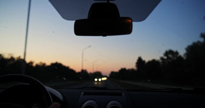 Car dashboard POV driving on country road with oncoming traffic bokeh headlights at sunset