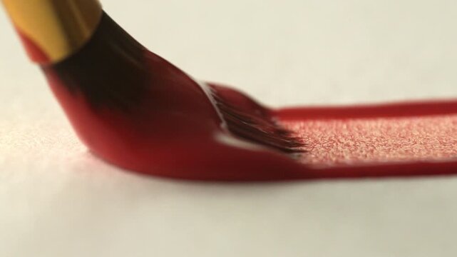 A close-up of a brush leaving a red line on white paper. The process of brush movement and paint texture during the creation of a drawing. Hobbies and leisure concepts
