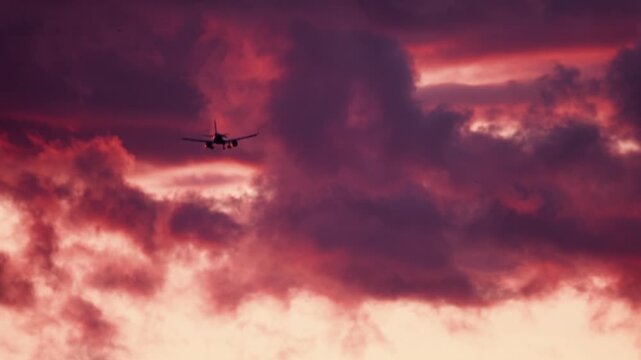 Airplane flying through colorful clouds during sunset