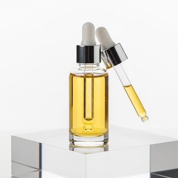 A mockup of a skincare product featuring a glass bottle with a dropper on a reflective surface showcasing the liquid product.