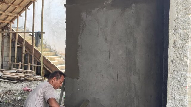 Skilled builder smoothing fresh cement plaster layer on unfinished brick wall