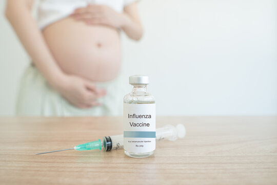 Influenza vaccine bottle and syringe on clinic table with blur pregnant woman background. Flu vaccine protects pregnant woman and infant from influenza virus infection, which can lead to pneumonia.