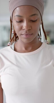 Vertical video: Adult African woman still lifting head and opening eyes in kitchen with beaded hair