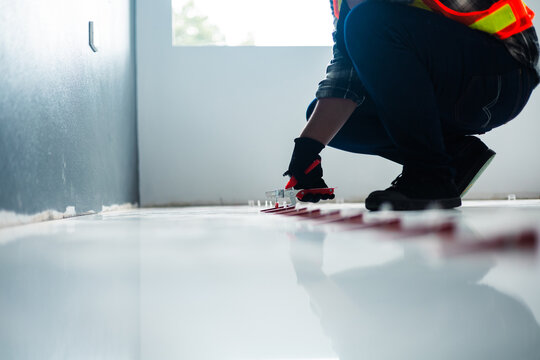 A worker in a safety vest and black gloves uses a tile leveling plier tool to adjust red wedges on a floor, installation and professional interior renovation.