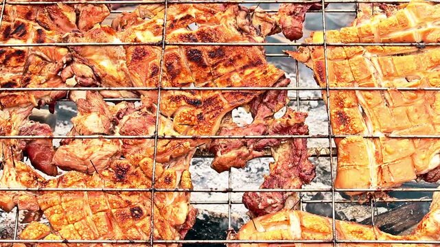 Traditional roasted pork belly with crispy skin cooking on a metal grill over charcoal.