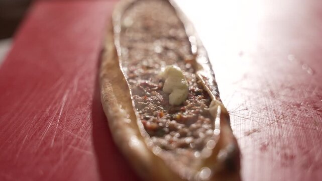 Hot Turkish pide with ground meat filling and melting butter on a red cutting board, fa01