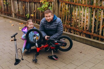 Obraz premium Father and daughter examine an upside down balance bike together before a ride. Shared bicycle maintenance turns everyday repairs into practical family learning.