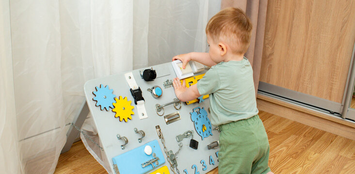 Two year old boy playing with busyboard at home. Fine motor skills development through safe exploration. Early childhood education through tactile learning and curiosity