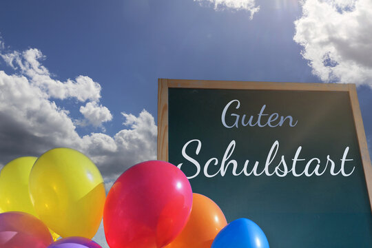 Tafel mit der Aufschrift GUTEN SCHULSTART vor blauem Himmel und Luftballons