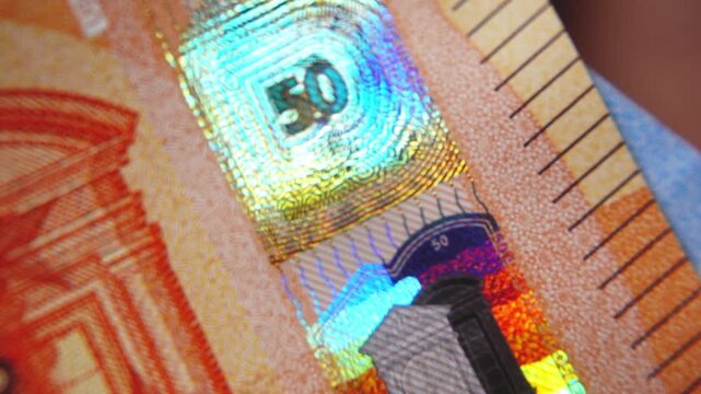 A close-up of the security strip with holographic emblems on the 50-euro banknote. Glowing security holograms on the 50-euro banknote. 4K macro slow motion video at 60 fps.