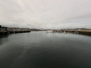 Fototapeta premium Panoramic Marina Harbor with Calm Water and Dramatic Cloudy Sky, Coastal City Waterfront in Northern Spain