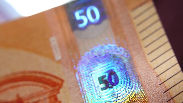 A close-up of the security strip with holographic emblems on the 50-euro banknote. Glowing security holograms on the 50-euro banknote. 4K macro slow motion video at 120 fps.