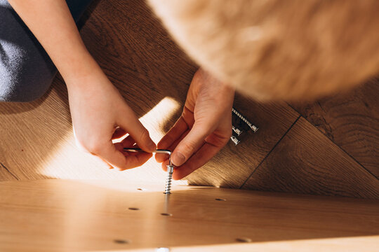 Close-up of kid's hands assembling flat pack furniture at home. DIY lifestyle scene showing home improvement, manual work, and furniture installation in natural light