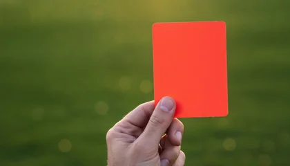 Referee hand holding red card over green soccer field background © Anna