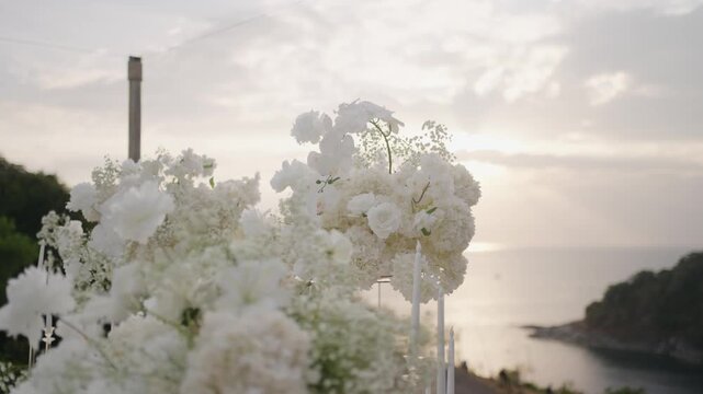 A dreamy, romantic composition featuring a lavish arrangement of delicate white flowers and baby's breath atop a modern clear acrylic stand, creating an elegant decor element for an outdoor wedding.