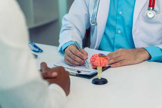 Neurologist discussing brain health and functions with a patient in a clinic.Doctor explaining neurological diagnosis using a human brain model during consultation.