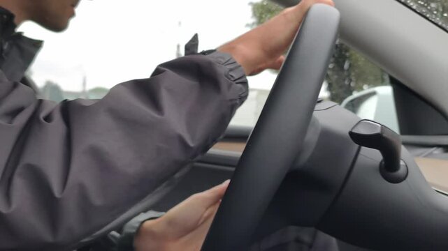 Driver hands maneuvering a steering wheel in a modern electric vehicle while wearing a smart ring. The rainy city background emphasizes the blend of advanced wearable tech and daily urban commuting.