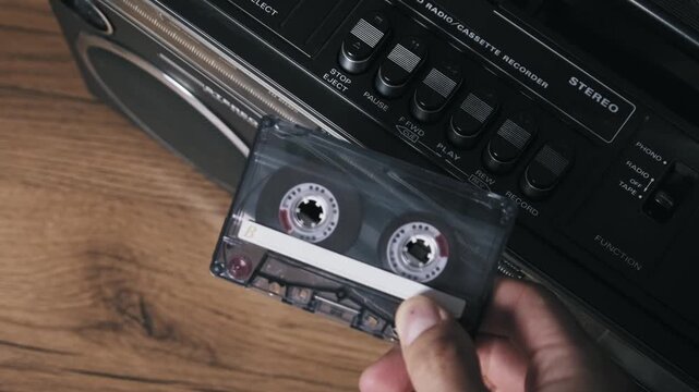 Close-up of a hand flipping a transparent audio cassette to side B in a retro player. The re-insertion and play button press highlight the vintage music listening experience.