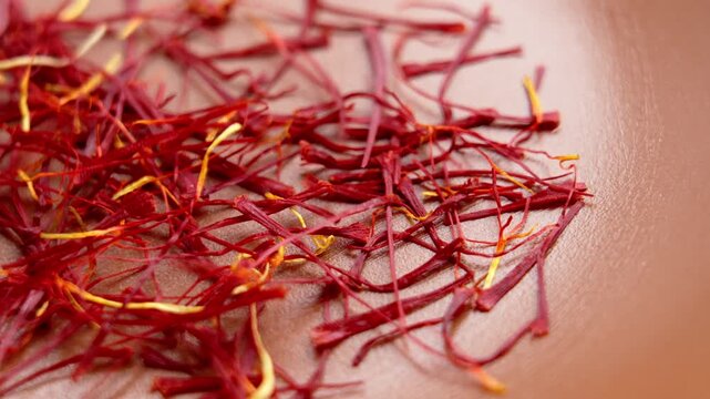 Fingers pick up premium saffron threads from the textured wooden surface of a kitchen bowl. Organic Mediterranean diet spicy seasoning. Macro
