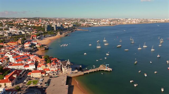 A drone reveals a bay filled with anchored sailboats near a coastal town