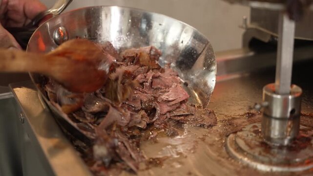 Professional chef preparing and scooping thinly sliced doner kebab meat in a restaurant kitchen, fa01