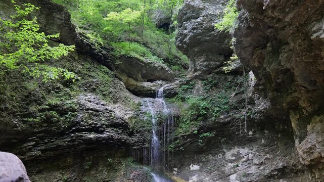 Scenic view of a natural waterfall cascading down a steep, mossy limestone rock bluff face deep inside a lush green Arkansas summer forest