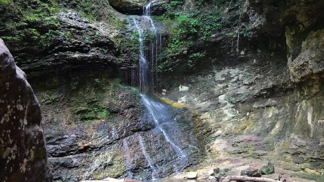 Scenic view of a natural waterfall cascading down a steep, mossy limestone rock bluff face deep inside a lush green Arkansas summer forest