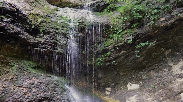 Scenic view of a natural waterfall cascading down a steep, mossy limestone rock bluff face deep inside a lush green Arkansas summer forest
