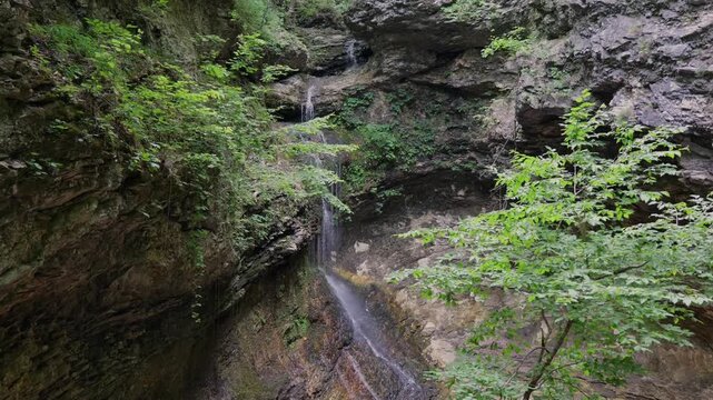 Scenic view of a natural waterfall cascading down a steep, mossy limestone rock bluff face deep inside a lush green Arkansas summer forest