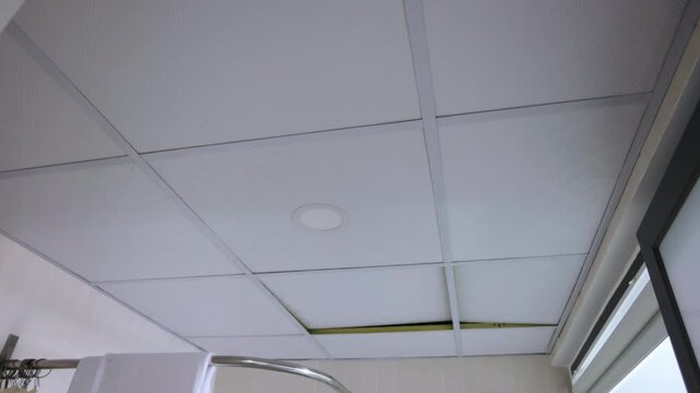 Suspended ceiling tiles moving up and down due to strong ventilation draft. Low angle view of office tiles shaking, concept of earthquake, paranormal activity, or poltergeist in the room
