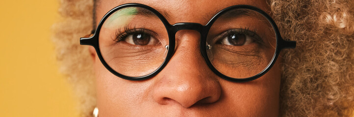 Close-up portret of girl in glasses, wearing brown top opening her eyes and looking at the camera isolated on orange background. Panoramic © Andrii Nekrasov