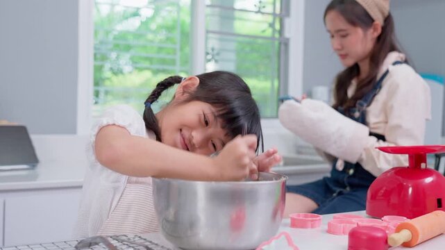 Sweet Home Baking Moments: Two young girls are deeply engrossed in their baking process. One is playfully mixing dough with her hands, a sweet smile on her face, while the other is looking.