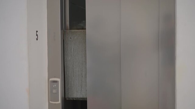 Empty stuck elevator with half-open doors between floors. Handheld.