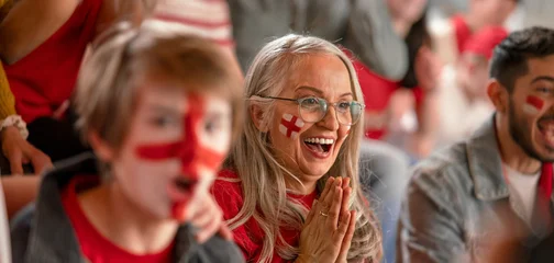 Excited senior woman football fan supproting English national team in live soccer match at stadium. © Halfpoint