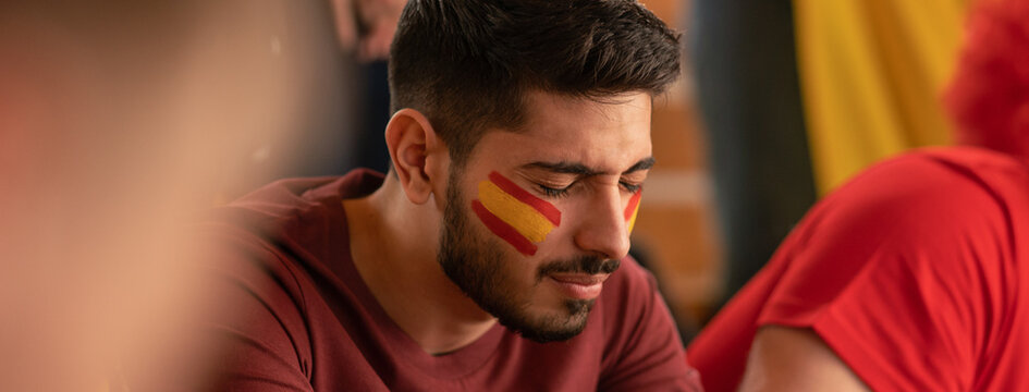 Worried football fans supporting spanish national team in live soccer match at stadium.