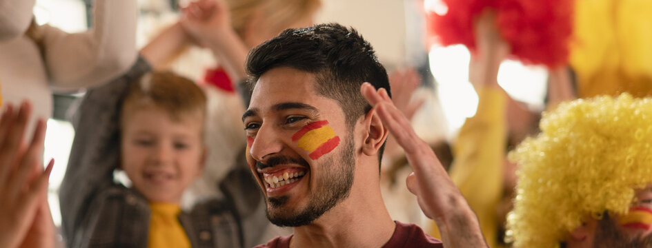 Excited, happy football fans supproting spanish national team in live soccer match at stadium.