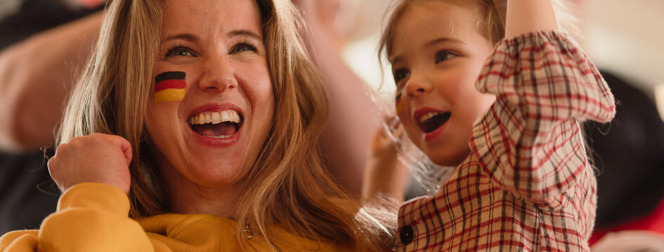 Excited football fans, mother with little daughter, supproting German national team in live soccer match at stadium.