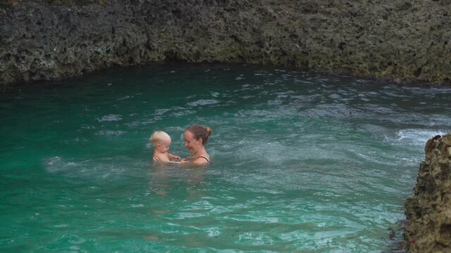 Mother and toddler swimming in beach rock pool by Caribbean Sea. Slow motion.