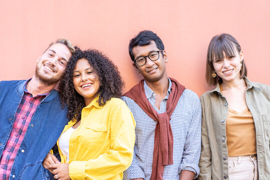 Smiling multiethnic friends posing together against a warm coral wall. Close-up portrait of millennials and gen z with relaxed confidence. Diversity concept