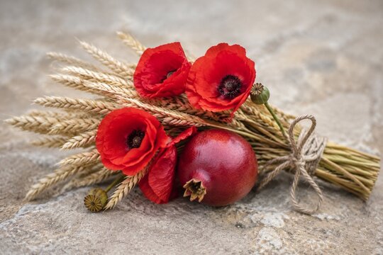 demeter. A harvest bouquet of wheat, red poppies, and a pomegranate tied with twine on stone. representing seasonal cycles and harvest abundance.