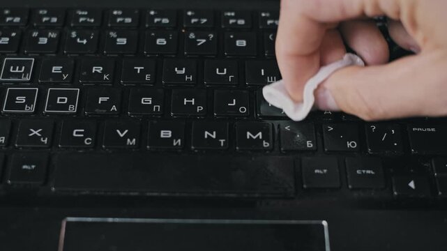 Close-up of a hand spraying disinfectant and wiping a dirty computer keyboard with a white cloth. The antibacterial procedure ensures a germ-free surface for safe office work.