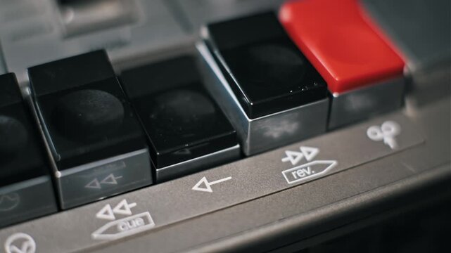Detailed macro view of a male finger pushing the play button on a vintage cassette tape deck. The black plastic key depresses to activate the mechanical functions.
