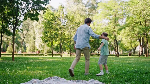 Happy father and little son play together on city park lawn