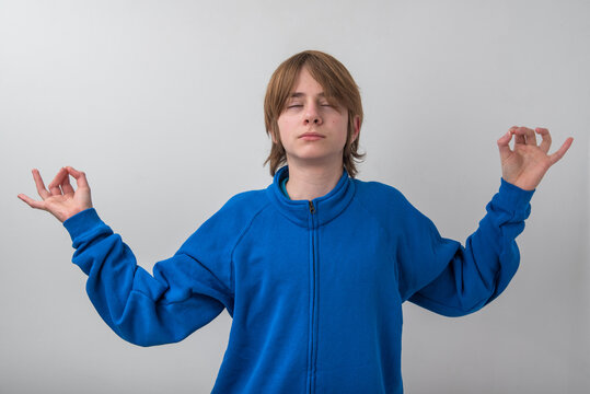 Young man meditating in studio with eyes closed, forming mudra with both hands, embodying calm, inner peace and mindful relaxation against a clean white background